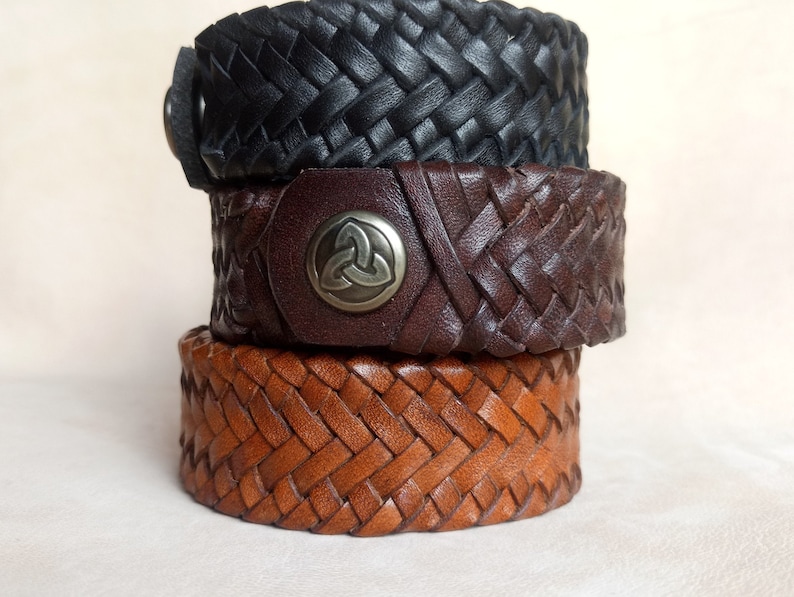 K&ouml;nnte beinhalten: Drei Lederarmb&auml;nder, die &uuml;bereinander gestapelt sind. Das obere Armband ist schwarz, das mittlere Armband ist braun mit einem Metall-Keltenknoten-Design und das untere Armband ist braun.