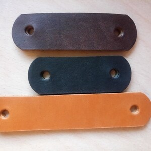 May include: Three leather straps with holes for attaching to a project. The straps are brown, black, and orange.