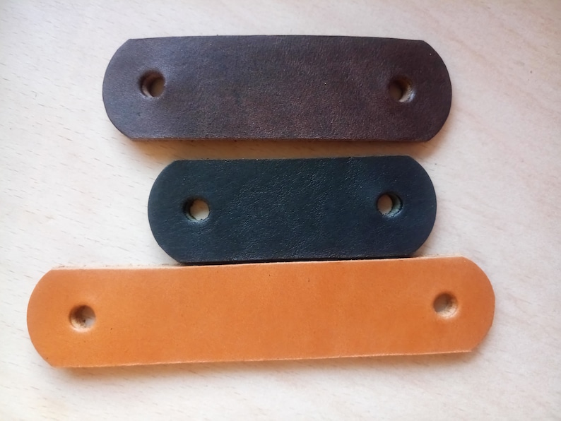 May include: Three leather straps with holes for attaching to a project. The straps are brown, black, and orange.