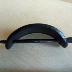 Op de afbeelding: Zwarte houten haarstick met een gebogen, halfronde houten stuk bevestigd aan het uiteinde. De stick is glad en gepolijst.