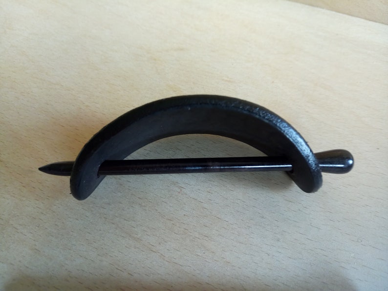 Op de afbeelding: Zwarte houten haarstick met een gebogen, halfronde houten stuk bevestigd aan het uiteinde. De stick is glad en gepolijst.