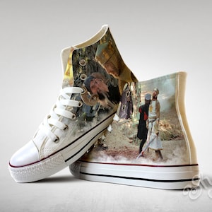May include: White high-top canvas sneakers with a printed image of a scene from the film Monty Python and the Holy Grail. The image features three characters, including King Arthur, a knight, and a man in a robe.