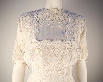 May include: A white lace dress with a high neckline and short sleeves. The dress is made of delicate lace with a floral pattern.