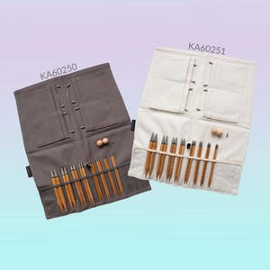 May include: Two sets of knitting needles in a roll-up case. The needles are made of bamboo and have metal tips. The cases are made of fabric and have a zipper closure. The case on the left is gray and the case on the right is white. The text "KA60250" is printed on the gray case and the text "KA60251" is printed on the white case.
