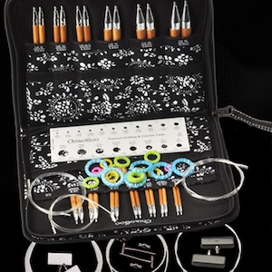 May include: A black zippered case with a white floral pattern contains a set of interchangeable knitting needles, circular needles, stitch markers, and a ruler. The case is open and the needles are visible. The needles are made of bamboo and have metal tips. The case also includes a ruler with measurements in inches and centimetres.