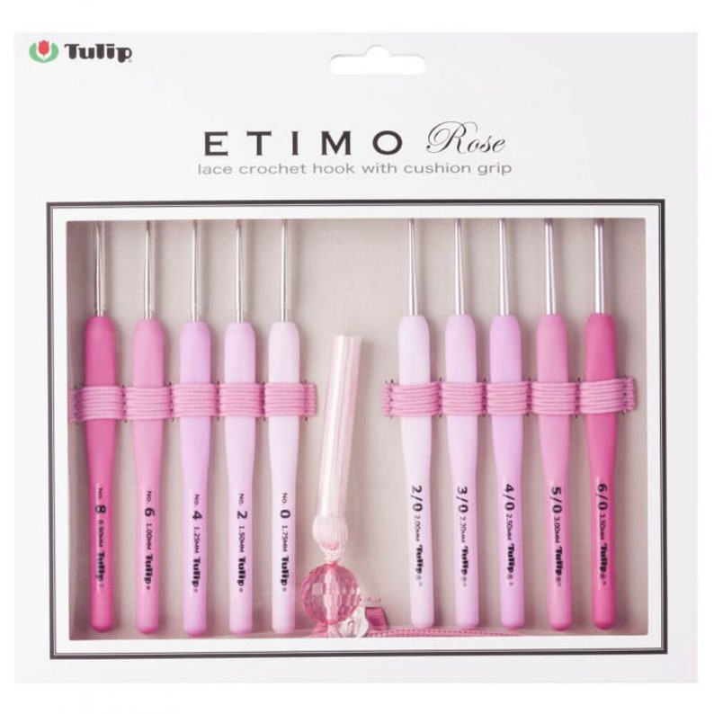 May include: A collection of pink crochet hooks with cushioned grips, presented in a white box. The hooks vary in shades of pink and are secured with pink elastic. The box is labelled "ETIMO Rose", and the hooks are for lace crochet.