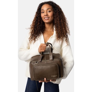 May include: A dark olive green leather handbag with a top handle and a front pocket. The bag has a rectangular shape and a zipper closure. The bag is held by a person wearing a white sweater and blue jeans.