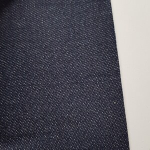 May include: A close-up of a dark blue denim fabric with a textured weave.