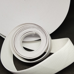 May include: White elastic band rolled up on a black surface. The elastic band is a flat, woven material with a textured surface.