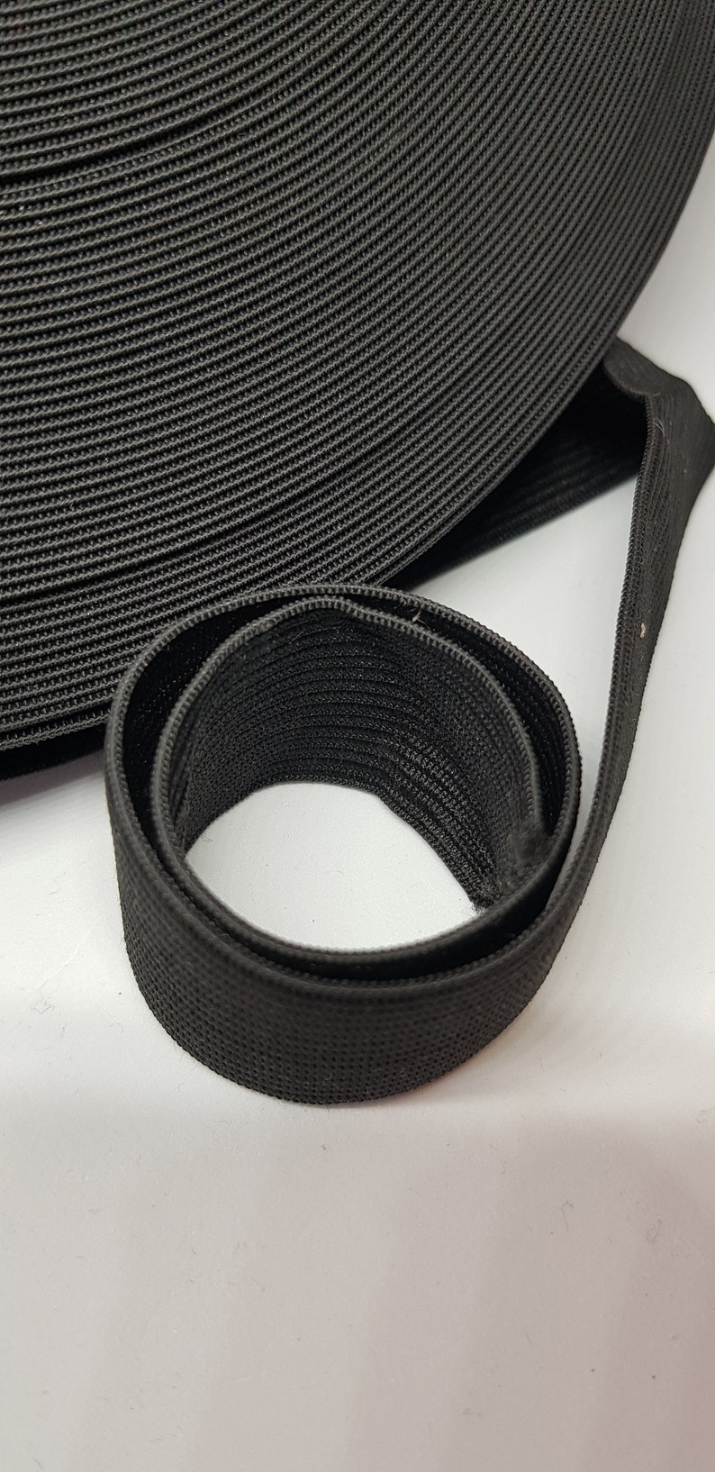 May include: Black elastic band, rolled up and folded, showing the texture of the fabric.