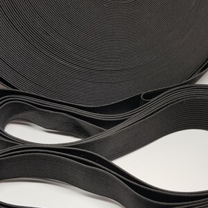 May include: A close-up of black elastic band rolled up. The elastic band is a woven material with a textured surface.