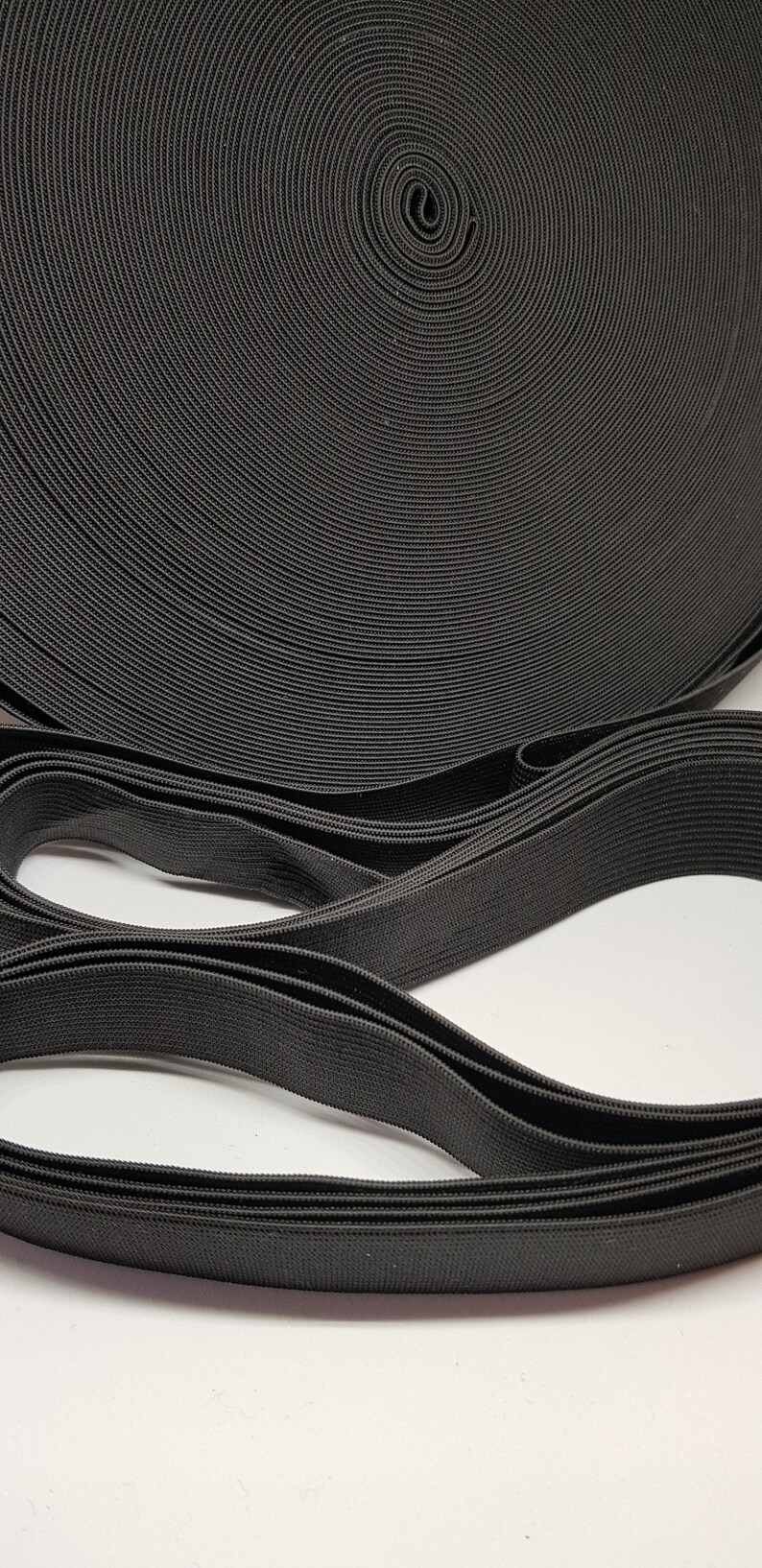 May include: A close-up of black elastic band rolled up. The elastic band is a woven material with a textured surface.