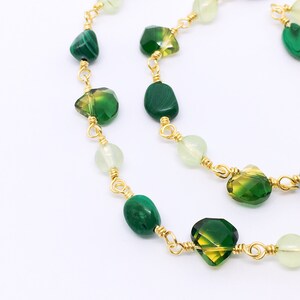 May include: A gold chain necklace with green and light green gemstone beads. The necklace features a variety of shapes and sizes of beads, including round, oval, and square.