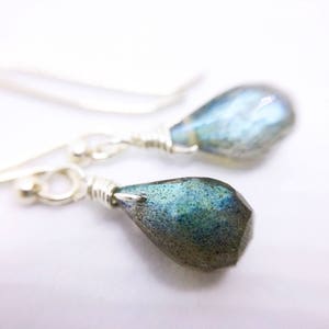 May include: A pair of silver dangle earrings with teardrop-shaped labradorite stones. The stones have a blue-green iridescent shimmer.