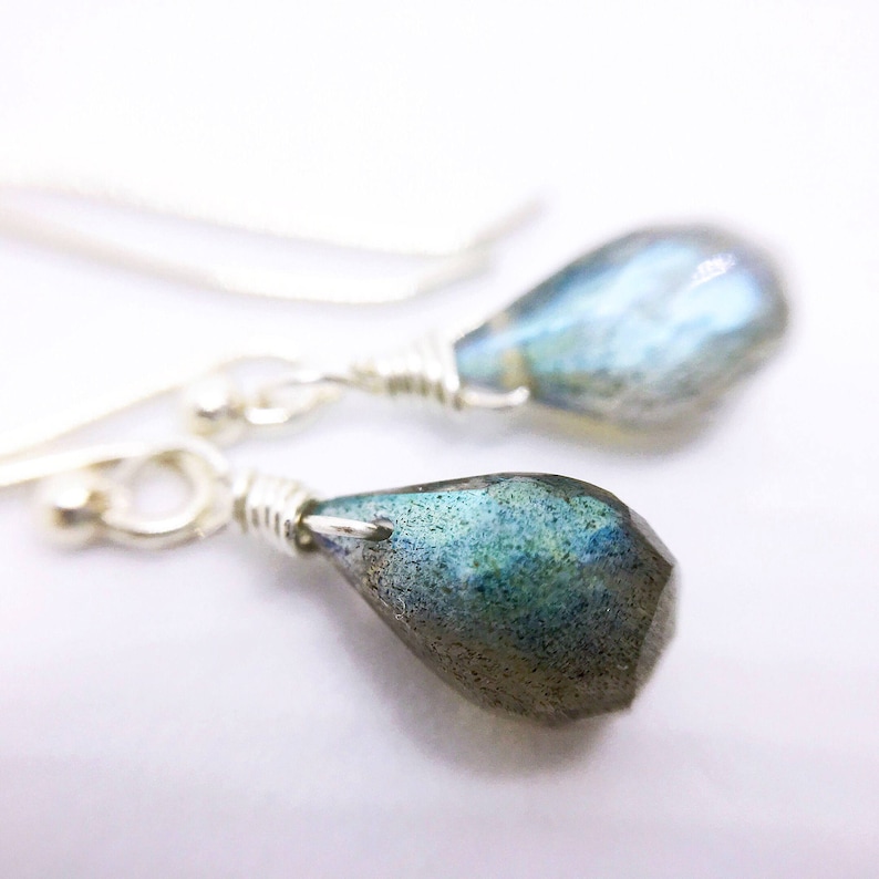 May include: A pair of silver dangle earrings with teardrop-shaped labradorite stones. The stones have a blue-green iridescent shimmer.