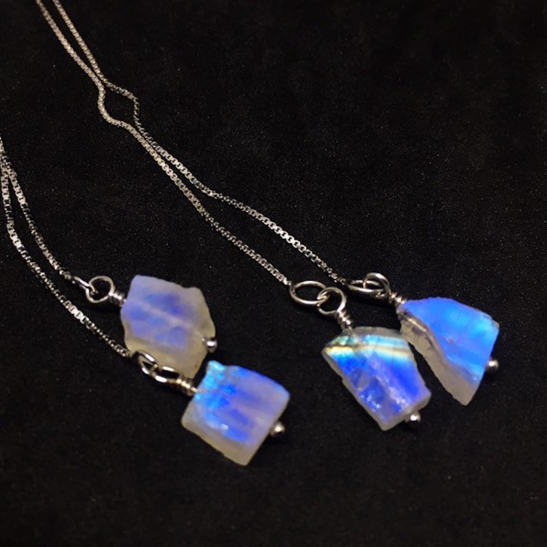 May include: A pair of silver chain earrings with iridescent blue moonstone pendants. The moonstone is a natural, raw, and irregular shape.