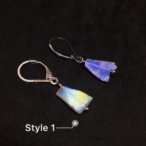 May include: A pair of silver earrings with iridescent blue and yellow gemstone drops. The earrings are in the style of a teardrop shape. The text "Style 1" is visible in the image.