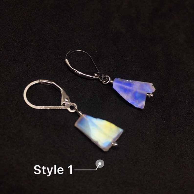 May include: A pair of silver earrings with iridescent blue and yellow gemstone drops. The earrings are in the style of a teardrop shape. The text "Style 1" is visible in the image.