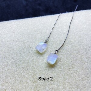 May include: A pair of silver dangle earrings with a white moonstone gemstone on each earring. The earrings are on a white background with the text "Style 2".