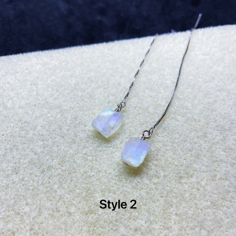 May include: A pair of silver dangle earrings with a white moonstone gemstone on each earring. The earrings are on a white background with the text "Style 2".
