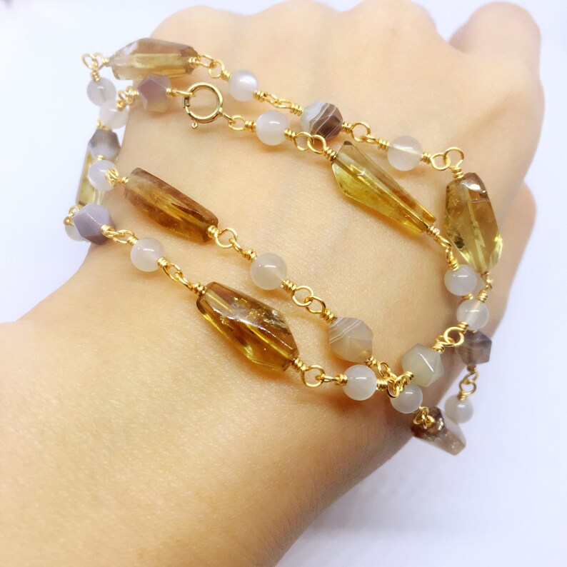 May include: A gold chain necklace with brown and white gemstone beads. The necklace is layered and features a variety of shapes and sizes of beads.