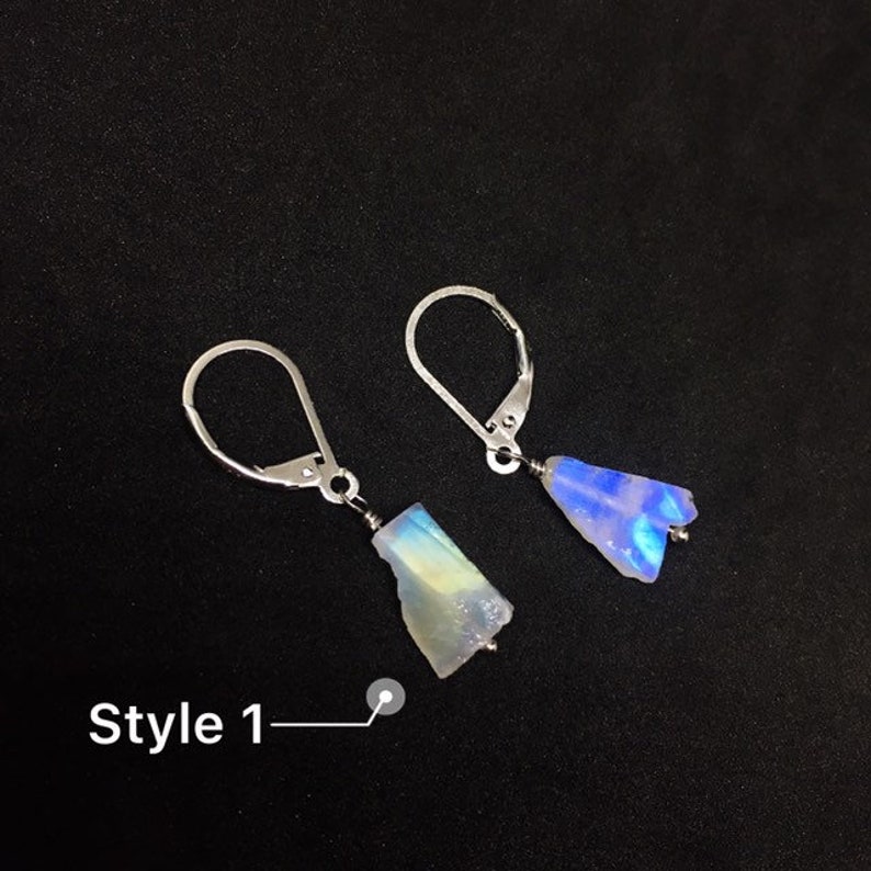 May include: A pair of silver earrings with iridescent blue and white gemstone accents. The earrings are in the style of a teardrop and a rectangle. The text "Style 1" is visible in the image.