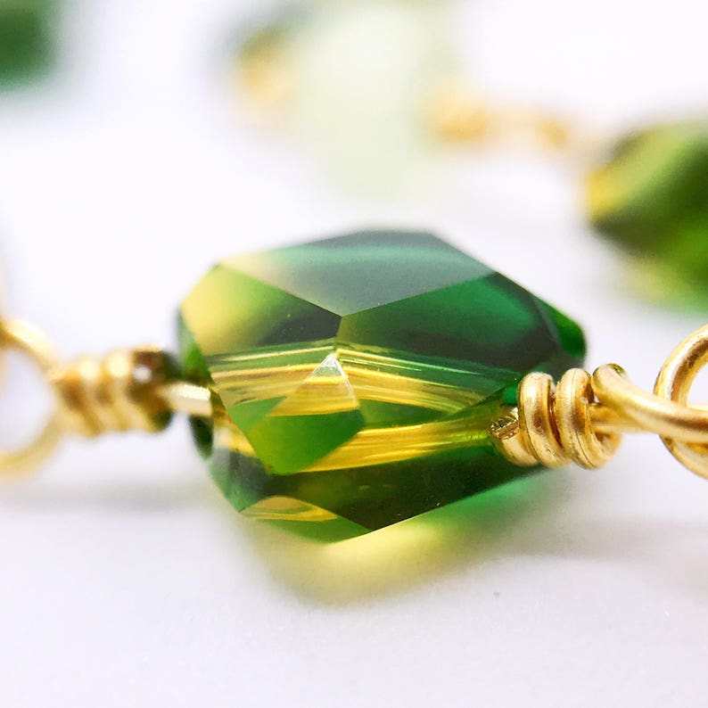 May include: A close-up of a green and yellow crystal bead with gold wire wrapped around it.