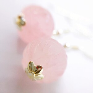May include: A pair of pink rose quartz earrings with gold flower accents. The earrings are made of natural stone and have a delicate, feminine look.