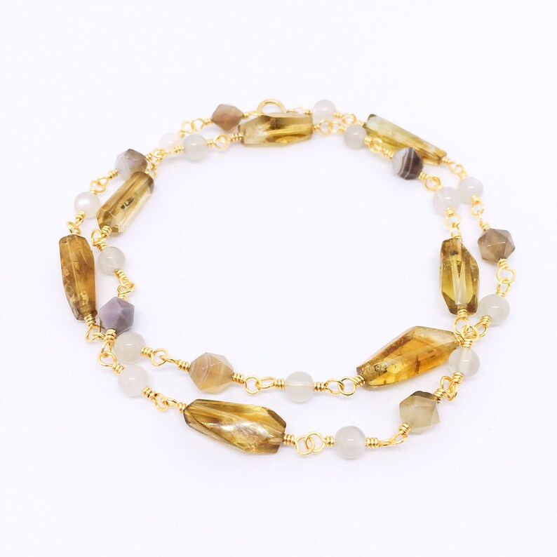 May include: A gold chain necklace with brown and white gemstone beads. The necklace features a double strand of beads with a variety of shapes and sizes.