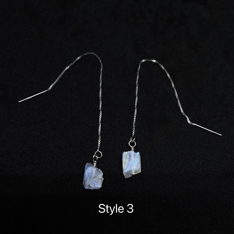 May include: A pair of silver dangle earrings with iridescent blue moonstone stones. The earrings are labeled "Style 3".