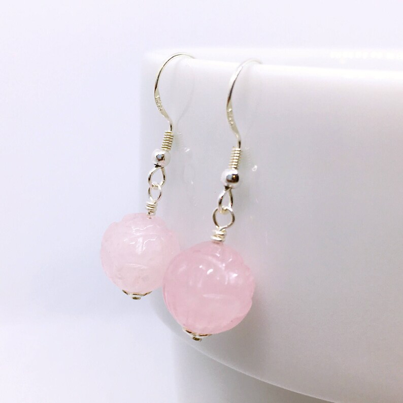 May include: A pair of silver dangle earrings with pink carved rose quartz beads. The earrings have a simple design and are perfect for everyday wear.