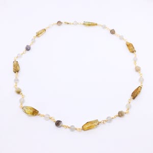 May include: A gold chain necklace with brown, gray, and white gemstone beads. The necklace is made with small, round beads and larger, rectangular beads.