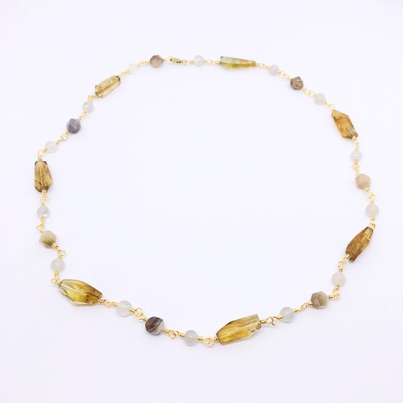 May include: A gold chain necklace with brown, gray, and white gemstone beads. The necklace is made with small, round beads and larger, rectangular beads.