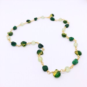 May include: A gold chain necklace with green and light green gemstone beads. The beads are various shapes and sizes.