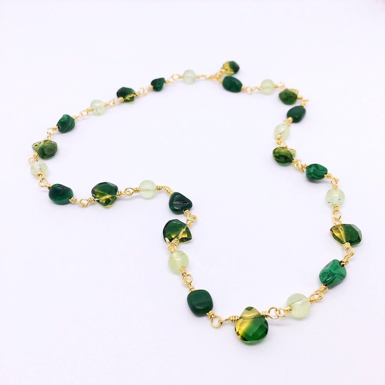 May include: A gold chain necklace with green and light green gemstone beads. The beads are various shapes and sizes.