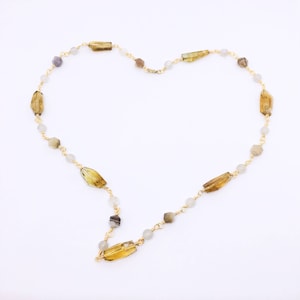 May include: A gold chain necklace with alternating light gray and brown rectangular beads. The necklace is arranged in a heart shape.