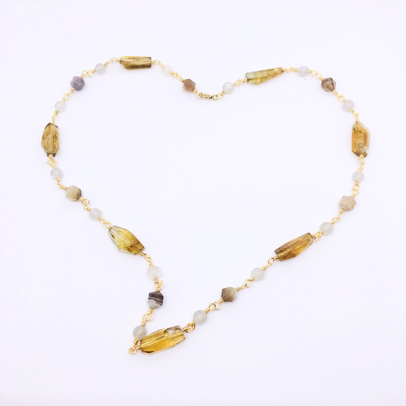 May include: A gold chain necklace with alternating light gray and brown rectangular beads. The necklace is arranged in a heart shape.