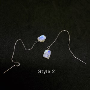 May include: A pair of silver dangle earrings with iridescent moonstone stones. The earrings are long and feature a delicate chain. The text "Style 2" is visible below the earrings.