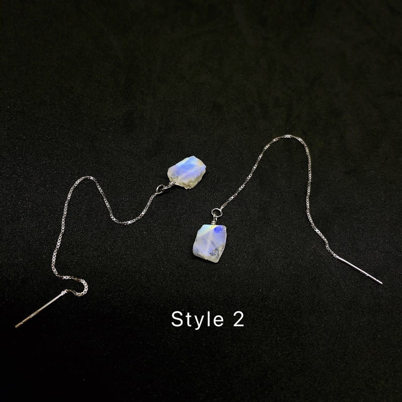 May include: A pair of silver dangle earrings with iridescent moonstone stones. The earrings are long and feature a delicate chain. The text "Style 2" is visible below the earrings.
