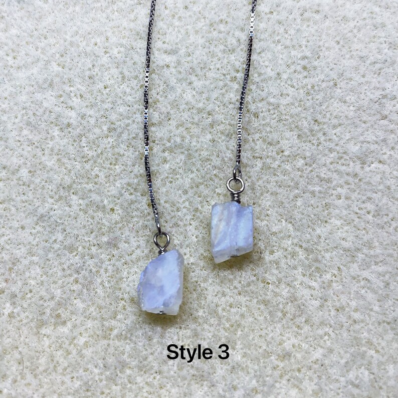 May include: A pair of silver chain earrings with a light blue, iridescent gemstone attached to each chain. The text "Style 3" is visible below the earrings.