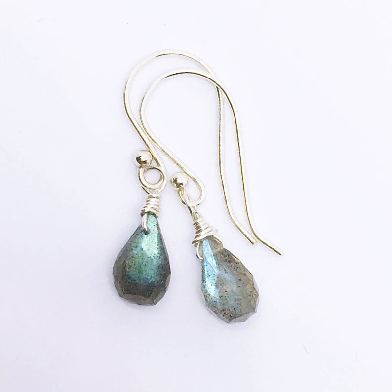 May include: A pair of silver dangle earrings with teardrop-shaped labradorite stones. The stones have a blue-green iridescent sheen.