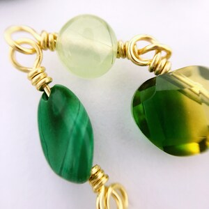 May include: Close-up of a gold wire wrapped bracelet with green and yellow gemstone beads. The beads are a light green, a dark green, and a yellow-green.