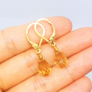 May include: Gold teardrop earrings with a faceted citrine gemstone. The earrings have a simple, elegant design.