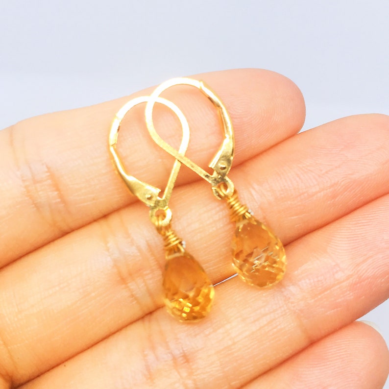 May include: Gold teardrop earrings with a faceted citrine gemstone. The earrings have a simple, elegant design.