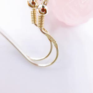 May include: Close-up of a silver earring with a twisted wire design. The earring has a small, round, silver charm with the number "30225" engraved on it.