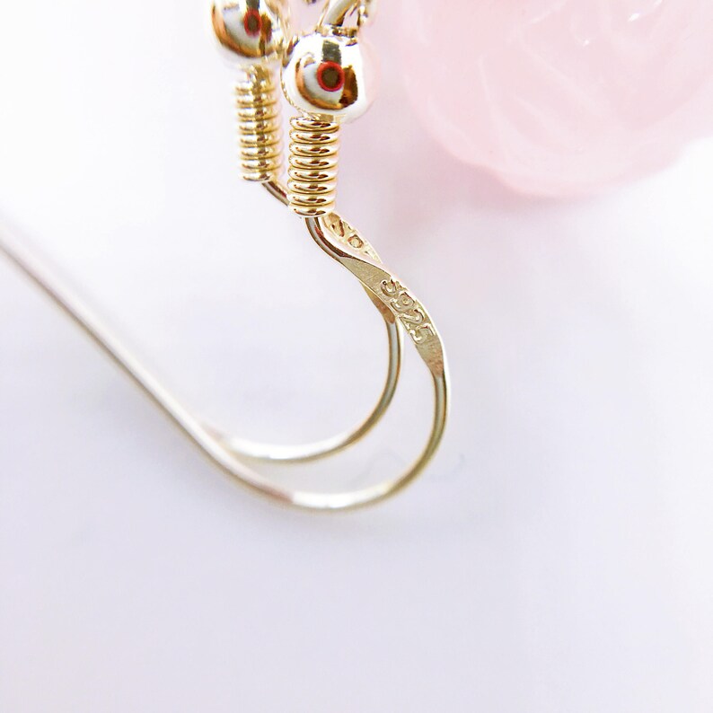 May include: Close-up of a silver earring with a twisted wire design. The earring has a small, round, silver charm with the number "30225" engraved on it.