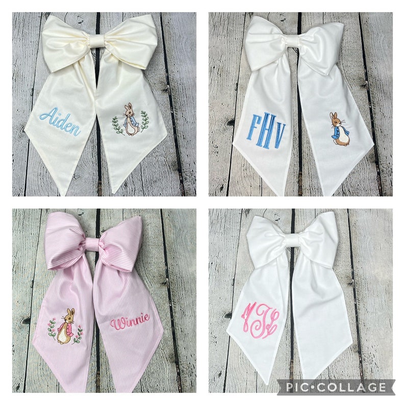 May include: Four white fabric hair bows with different embroidered designs. The top left bow has the name "Aiden" and a Peter Rabbit illustration. The top right bow has the monogram "FHV". The bottom left bow has the name "Winnie" and a Peter Rabbit illustration. The bottom right bow has the monogram "MJ".
