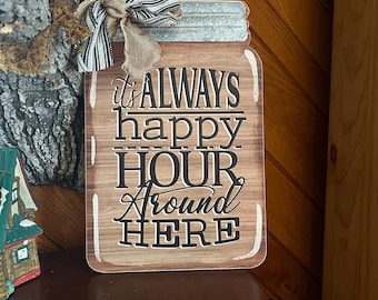 Puede incluir: Cartel de madera con forma de tarro con el texto "It's ALWAYS happy HOUR AROUND HERE" en negro. El cartel tiene una tapa de metal y un lazo de tela a rayas y arpillera.