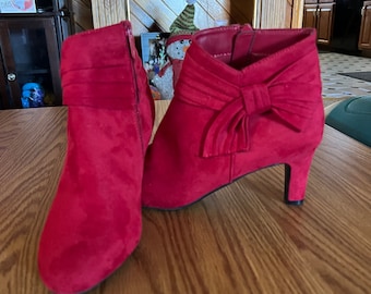 May include: A pair of red suede ankle boots with a bow on the top of each boot. The boots have a low heel.