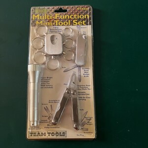 May include: A multi-function mini-tool set in a clear plastic package. The set includes a flashlight, key rings, a knife, pliers, a screwdriver, and other tools. The package has the text "Multi-Function Mini-Tool Set" and "Team Tools".